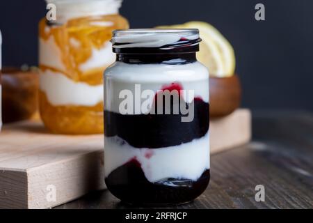 Yogurt a base di latte fresco con aggiunta di marmellata dolce di limone, fragole e mirtilli, confezionato in vasetti di vetro yogurt alla bacche Foto Stock