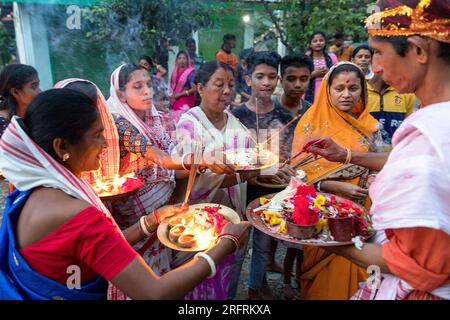Signore locali in abiti indù tradizionali indiani, che tengono in mano candele e regali per gli dei durante una cerimonia religiosa ad Assam, in India Foto Stock
