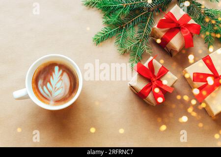 Sfondo natalizio e Capodanno. Rami dell'albero di Natale, scatole regalo con fiocchi rossi, tazza di caffè su sfondo di carta artigianale. Vista dall'alto, piatta Foto Stock