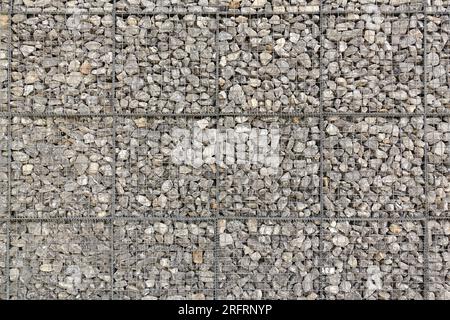 Sezione di una grande parete in gabbione, realizzata con pietre di ghiaia grigie sciolte e reti metalliche Foto Stock