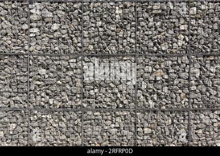 Sezione di una grande parete in gabbione, realizzata con pietre di ghiaia grigie sciolte e reti metalliche Foto Stock