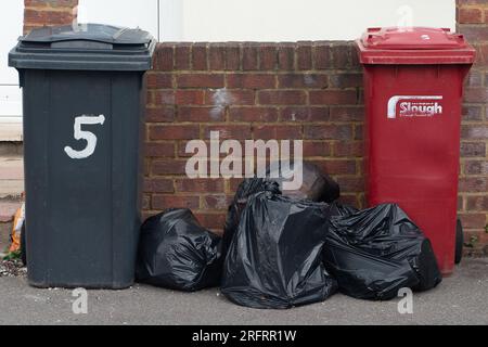 Slough, Berkshire, Regno Unito. 3 agosto 2023. Bidoni e sacchetti neri fuori casa a Slough, Berkshire. Slough Borough Council (SBC) ha recentemente introdotto una modifica alle collezioni di cestini dei residenti al fine di incoraggiare i residenti a riciclare di più. I contenitori grigi con rifiuti generici, compreso il cibo, vengono ora raccolti una volta ogni due settimane piuttosto che una volta alla settimana, con il riciclaggio in contenitori rossi, che vengono raccolti nella settimana alternata. Alcuni residenti di Slough stanno ora segnalando problemi con i vermi e gli odori di rifiuti non raccolti lasciati sulle strade, che probabilmente peggioreranno solo una volta che le temperature Foto Stock