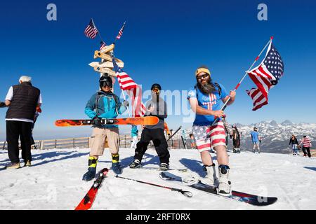Mammoth Lakes, CA. 4 luglio 2023. Tre uomini con bandiere americane si preparano a fare snowboard in cima alla stazione sciistica di Mammoth Mountain sotto un cielo estivo blu. Foto Stock