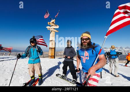 Mammoth Lakes, CA. 4 luglio 2023. Tre uomini con bandiere americane si preparano a fare snowboard in cima alla stazione sciistica di Mammoth Mountain sotto un cielo estivo blu. Foto Stock
