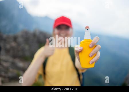 Giovane donna viaggia spruzzando repellenti per insetti sulla pelle con una bottiglia spray durante l'escursione in cima alla natura. Protezione della pelle contro il morso di insetti. Foto Stock