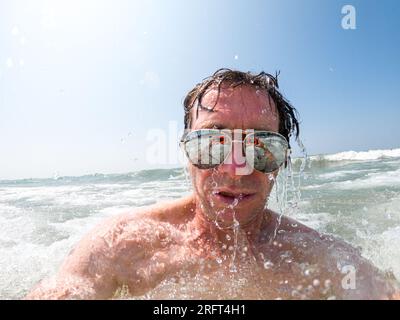 Gocciolamento d'acqua dall'uomo che nuota nel lago con gli occhiali da sole Foto Stock