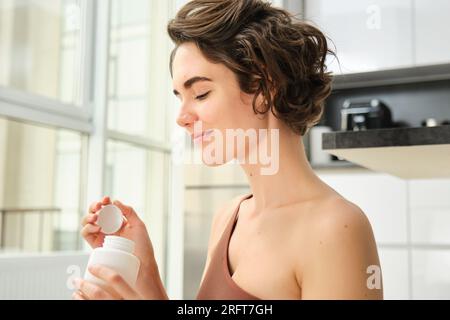 Ritratto di giovane sportiva, fitness girl prende vitamine, gemme per un corpo sano e in forma, allenamento in casa, sorride felicemente Foto Stock