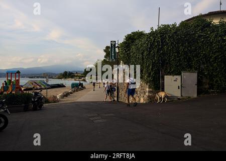 Passeggiata panoramica accanto a una riva del lago delimitata da un parco su un tramonto nuvoloso Foto Stock