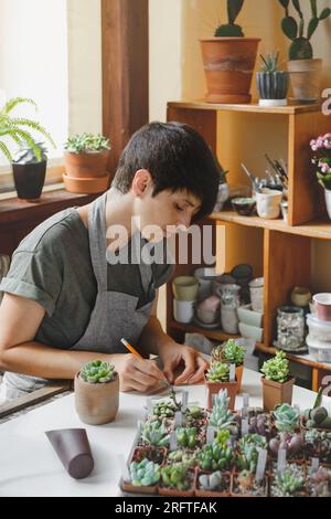 Etichettatura di piante grasse in vasi in vendita. Donna laorista che scrive titoli per piante da casa nella propria collezione. Concetto di hobby e piccola impresa. Repotting Foto Stock