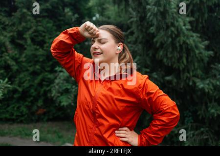 Donna con corpo extra-size che si rilassa dopo una sessione di allenamento all'aperto. Donna in abbigliamento sportivo che si prende una pausa dall'esercizio fisico. Foto Stock