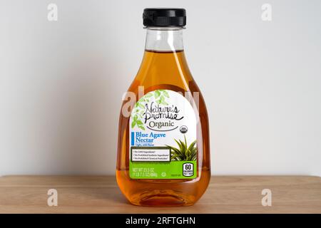Bottiglia di nettare di agave blu organico del marchio Nature's Promise su sfondo bianco e legno con spazio per la copia Foto Stock