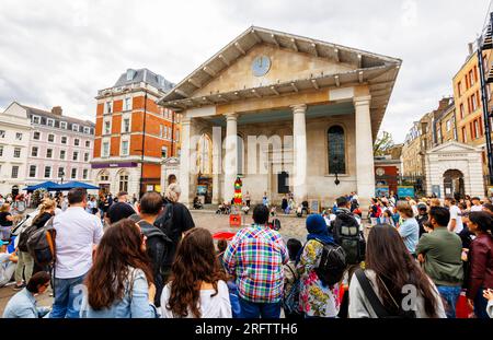 Gli spettatori guardano e ammirano un tradizionale artista di strada nella piazza presso la Chiesa di St Paul a Covent Garden nel West End di Londra, WC2 Foto Stock