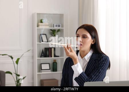 Donna che usa un portabicchieri lungo per fumare sul posto di lavoro in ufficio Foto Stock
