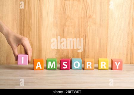 Donna che aggiunge cubo con lettera i per fare una frase che mi dispiace al tavolo di legno, primo piano. Spazio per il testo Foto Stock