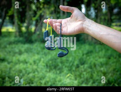 Due paia di cuffie sportive a conduzione ossea. Dispositivi audio che reggono le mani su sfondo verde tenue. Foto Stock