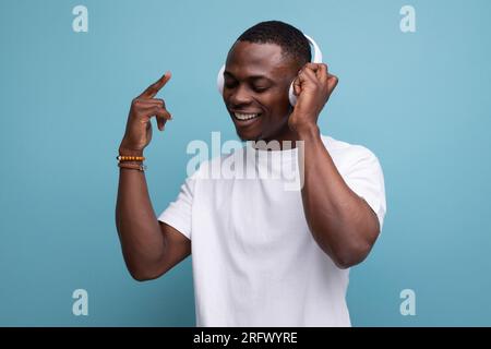 adorabile uomo africano del 30s ben curato con taglio corto in t-shirt bianca e musica in cuffia Foto Stock