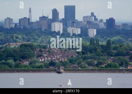 I membri del Bartley Sailing Club sull'acqua del Bartley Reservoir sono incorniciati dalla città di Birmingham, come visto da Frankley, Worcestershire, sette miglia a sud-ovest di Birmingham. Data foto: Domenica 6 agosto 2023. Foto Stock