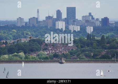 I membri del Bartley Sailing Club sull'acqua del Bartley Reservoir sono incorniciati dalla città di Birmingham, come visto da Frankley, Worcestershire, sette miglia a sud-ovest di Birmingham. Data foto: Domenica 6 agosto 2023. Foto Stock