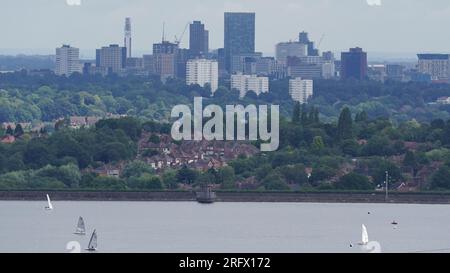 I membri del Bartley Sailing Club sull'acqua del Bartley Reservoir sono incorniciati dalla città di Birmingham, come visto da Frankley, Worcestershire, sette miglia a sud-ovest di Birmingham. Data foto: Domenica 6 agosto 2023. Foto Stock