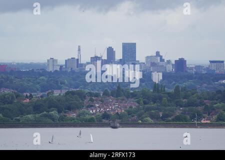 I membri del Bartley Sailing Club sull'acqua del Bartley Reservoir sono incorniciati dalla città di Birmingham, come visto da Frankley, Worcestershire, sette miglia a sud-ovest di Birmingham. Data foto: Domenica 6 agosto 2023. Foto Stock