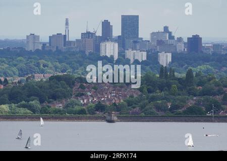 I membri del Bartley Sailing Club sull'acqua del Bartley Reservoir sono incorniciati dalla città di Birmingham, come visto da Frankley, Worcestershire, sette miglia a sud-ovest di Birmingham. Data foto: Domenica 6 agosto 2023. Foto Stock