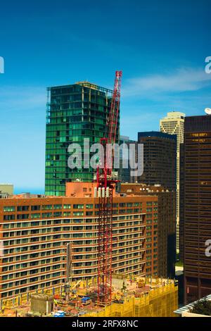 Vista maestosa di una gru rossa alta che opera contro un cielo blu brillante. Ombre e riflessi e una prospettiva impressionante aggiungono un tocco di interesse visivo. Foto Stock