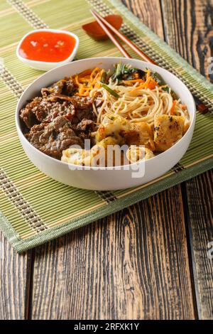 Ciotola di tradizionale insalata di noodle vietnamita Bun Bo Nam Bo, con manzo, spaghetti di riso, erbe fresche, verdure sott'aceto e salsa di pesce primo piano sul tabl Foto Stock