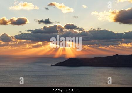 Il suggestivo tramonto sul mare con raggi del sole dalle sfumature arancioni, le nuvole davanti al sole creano raggi di luce e ombre chiaramente visibili Foto Stock