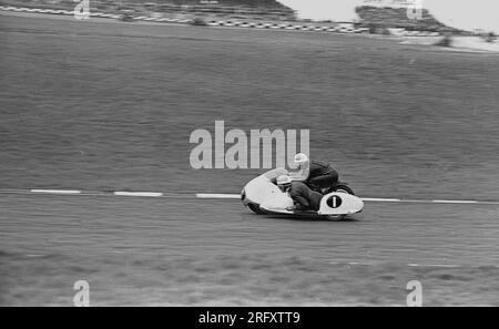 Anni '1960, storico, corse di sidecar di quest'epoca, una moto con sidecar, una moto a 3 ruote all'aperto su un circuito di gara, Inghilterra, Regno Unito. Viaggiando ad alta velocità in curva, le corse in sidecar sono l'unica forma di sport motoristico in cui il passeggero e il conducente guidano il veicolo e sono stati visti per la prima volta sull'Isola di Man nelle gare TT nei primi anni '1920 Foto Stock