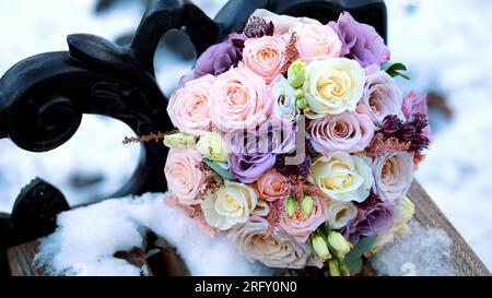 primo piano, bellissimo bouquet di rose, latticini bianchi e lilla. Il bouquet si trova su una panchina innevata nel parco. matrimonio invernale. Foto di alta qualità Foto Stock