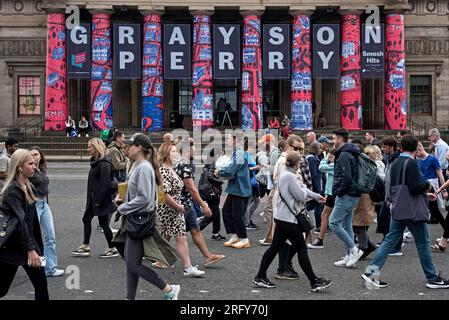 Pedoni su Princes Street Walk vicino alla Royal Scottish Academy che pubblicizza la mostra di Grayson Perry, parte del Festival di Edimburgo del 2023. Foto Stock