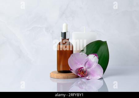 Primo piano del siero del viso. Una bottiglia di vetro con contagocce. Olio aromatico per massaggi su fondo di marmo grigio e fiore di orchidea vicino. Cosmetici naturali biologici spa Foto Stock