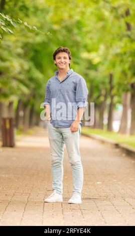 Ritratto di un uomo giovane e ben vestito in piedi fuori e sorridente alla luce del sole Foto Stock