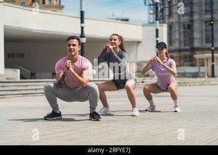 Tre amici sportivi che fanno squat in città. Ripresa con visuale dall'angolo basso Foto Stock