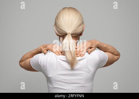 Donna bionda irriconoscibile che massaggia le spalle, vista posteriore Foto Stock