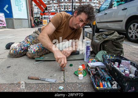 L'artista ben Wilson, che crea piccoli dipinti su gomma da masticare sul marciapiede, discute il suo lavoro con gli onlookers, North London, Regno Unito Foto Stock