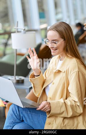 Studentessa felice che salta la mano guardando l'apprendimento ibrido dei notebook. Verticale Foto Stock