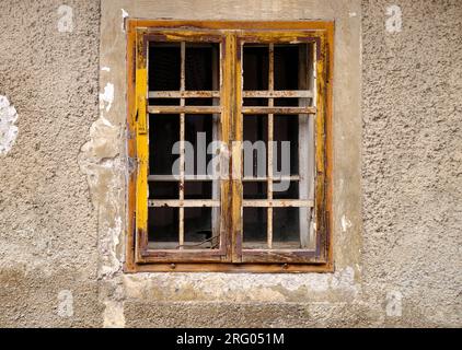 Cattura minimalista di una singola finestra rurale su una parete grigia testurizzata con peeling in cemento. Finestra semplice con telaio giallo e montanti Foto Stock