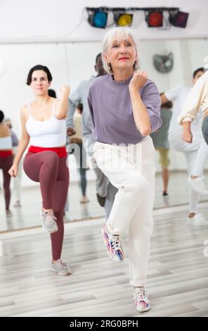 Giovane donna allegra imparando una nuova danza moderna nella lezione di danza di gruppo Foto Stock