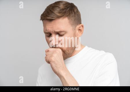 L'uomo malato con sintomi influenzali sente il disagio tosse a causa di malattia isolato su sfondo grigio studio Foto Stock