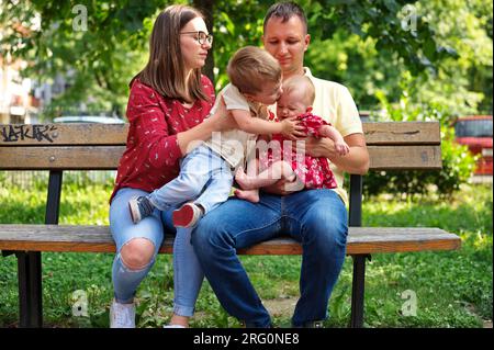 Famiglia con due bambini seduti su una panchina nel parco Foto Stock