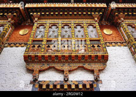 Guardando verso una tradizionale finestra a cavalletto in legno dipinta che si proietta dalla parete in muratura di un edificio sul terreno di Punakha Dzong in Bhutan. Foto Stock