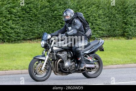 Whittlebury, Northants., UK - 6 agosto 2023. Uomo che indossa pelli da moto nere in sella a una Suzuki nera attraverso un villaggio inglese. Foto Stock