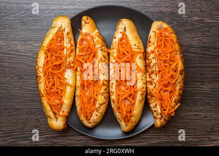 Gustosi hot dog su un piatto nero su uno sfondo di legno. Vista dall'alto, spazio di copia Foto Stock