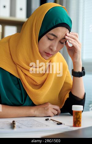 Donna musulmana stressata che soffre di mal di testa dopo aver lavorato al progetto per tutto il giorno Foto Stock