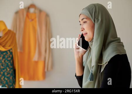 Donna musulmana matura sorridente che parla al telefono con un cliente felice Foto Stock