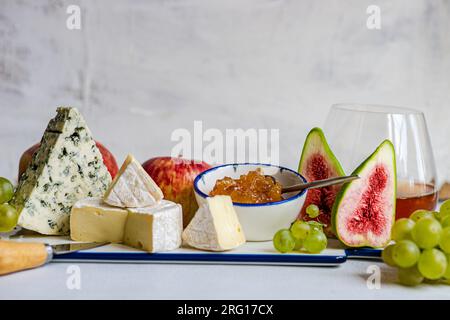 Spuntini squisiti assortiti con diversi tipi di formaggio e dolci serviti su un piatto di ceramica con uva, mela e fichi a tavola Foto Stock