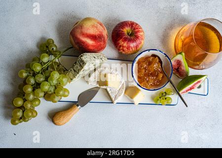 Dall'alto, squisiti spuntini assortiti con diversi tipi di formaggio e dolci serviti su un piatto di ceramica con uva, mela e fichi in tavola Foto Stock