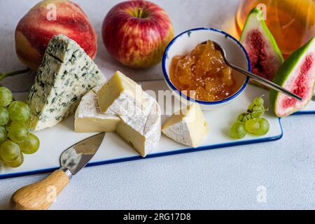 Dall'alto, squisiti spuntini assortiti con diversi tipi di formaggio e dolci serviti su un piatto di ceramica con uva, mela e fichi in tavola Foto Stock