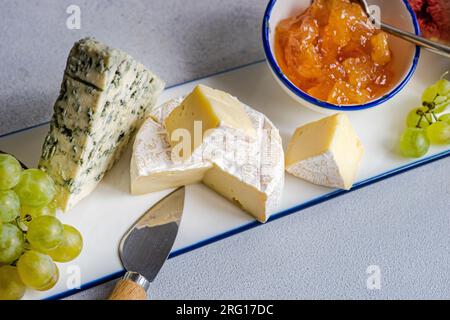 Dall'alto, squisiti spuntini assortiti con diversi tipi di formaggio e dolci serviti su un piatto di ceramica con uva Foto Stock